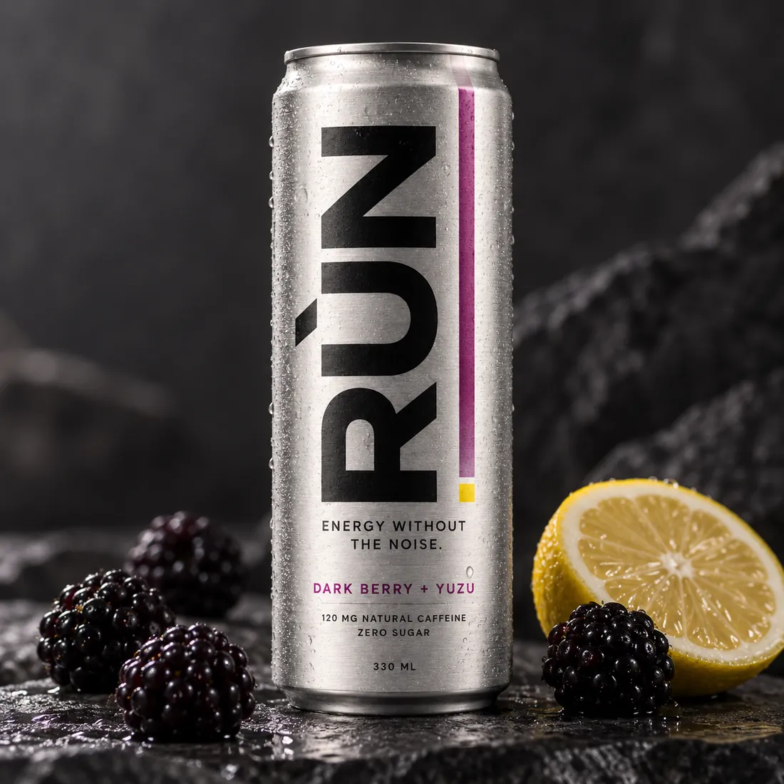 Rùn can beside blackberries and a halved citrus on dark slate
